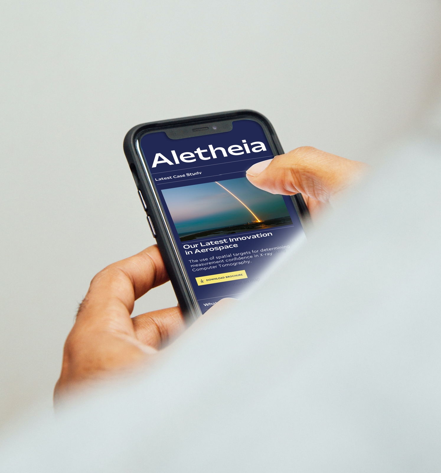 A hand holds a mobile phone looking at the Alethia site.