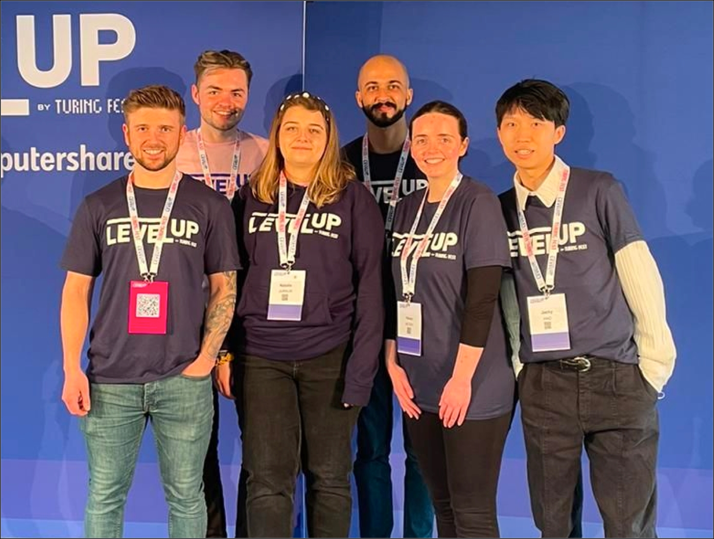 A group photo of 5 attendees smiling at the camera, wearing ‘Level Up’ promotional t-shirts and event lanyards.