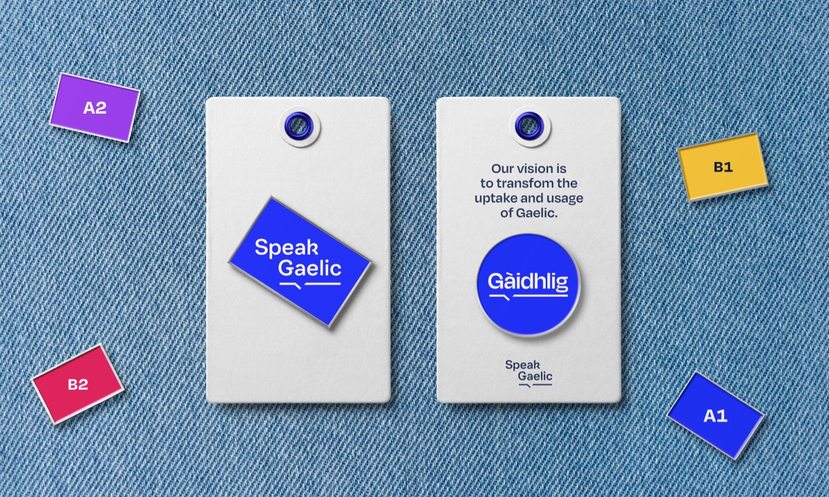 A variety of SpeakGaelic pin badges are displayed on a blue denim background