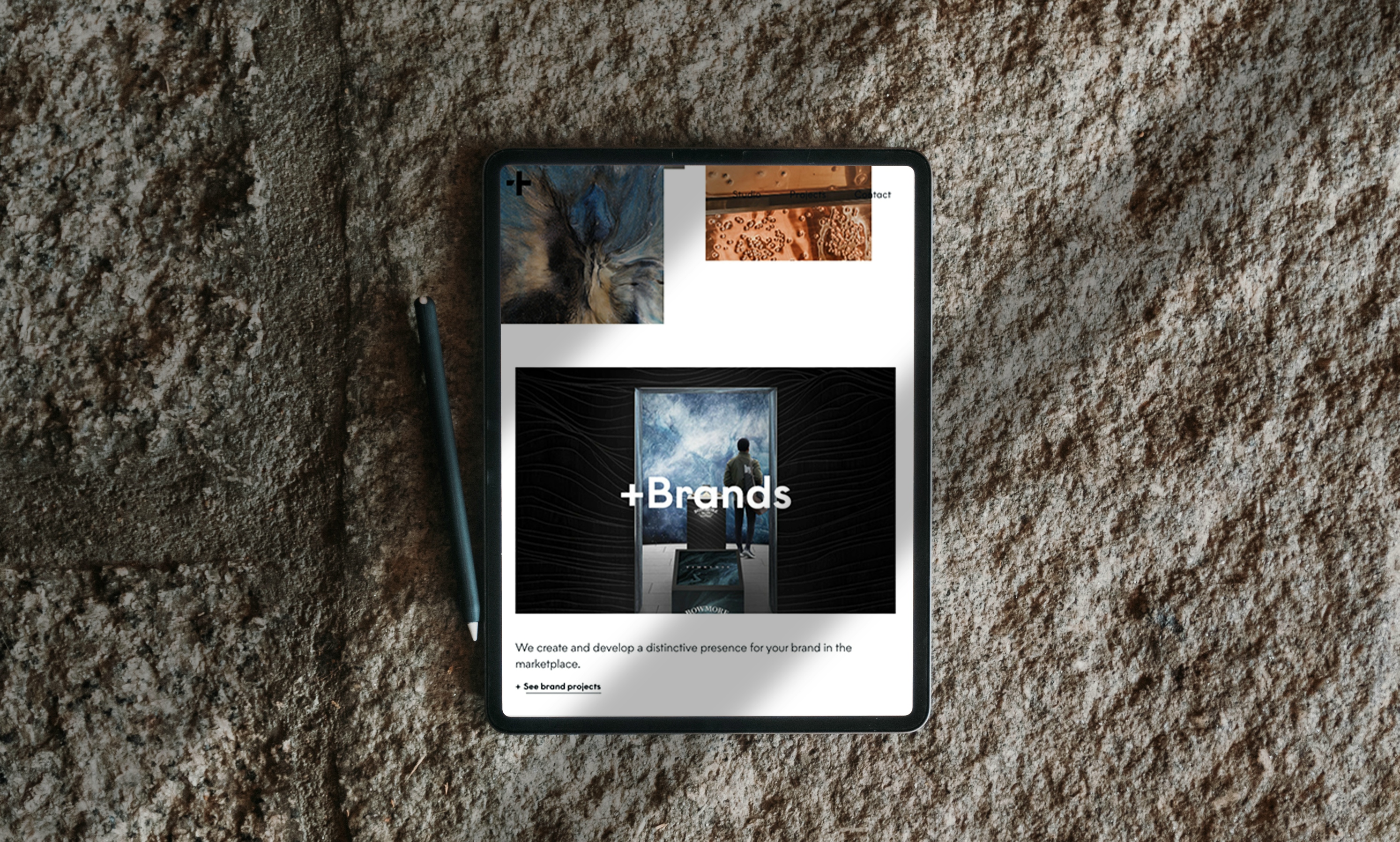 An image of sandstone with a tablet and pencil in the foreground. The tablet has a page on it. The main image is black with a door in it. Inside the door is a man looking on a sky background. “+Brands” is in white over the door. Under the image “We create and develop a distinctive presence for your brand in the marketplace”. There is a link under this stating “See brand products”