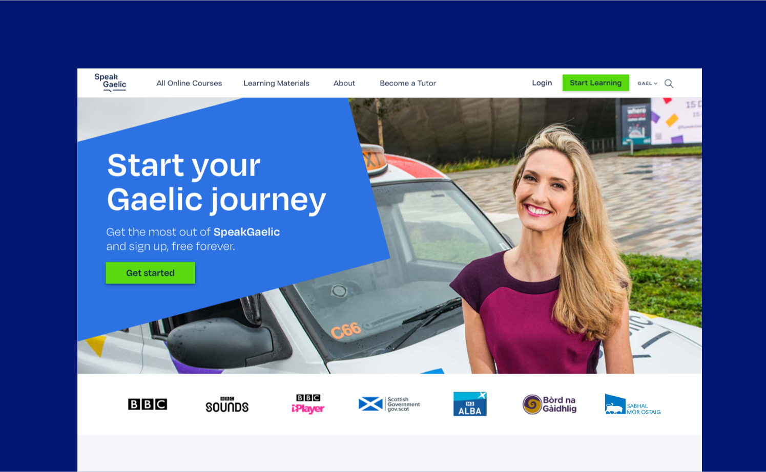 The SpeakGaelic homepage sits on a dark blue background. The SpeakGaelic homepage features Joy Dunlop and there is a large blue confetti piece stating “Start your Gaelic journey”. The SpeakGaelic partner logos are also featured.